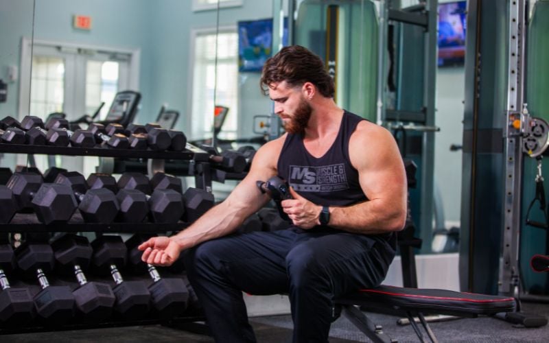 Male athlete wearing a black tank top using a therapy fun on his bicep.