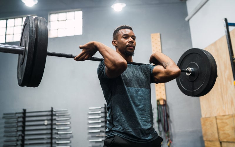 Man doing barbell front squat in Crossfit-style gym.