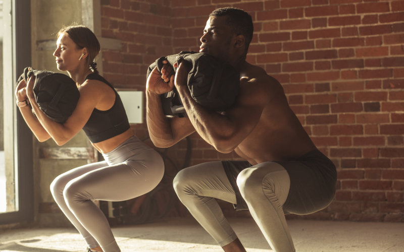 Man and woman doing front squats with sandbags. 
