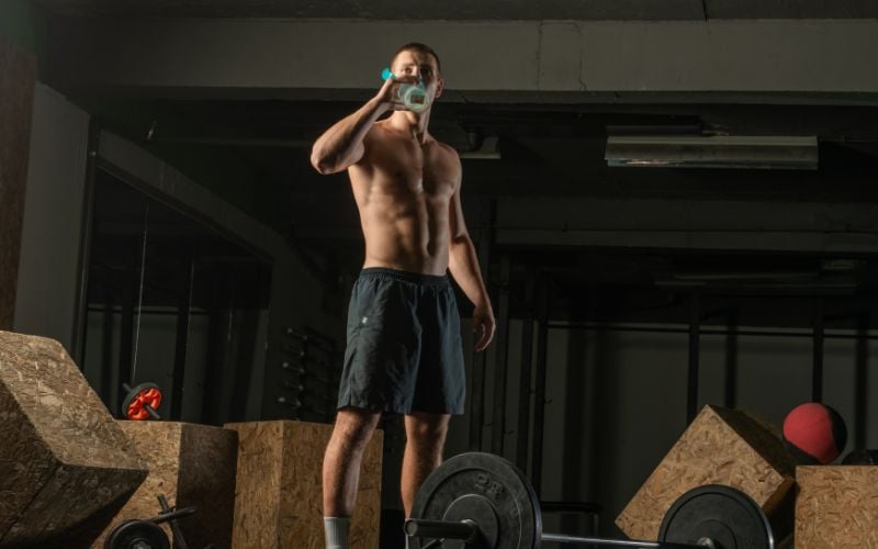 Muscular man taking a break from a hardcore workout while drinking water.