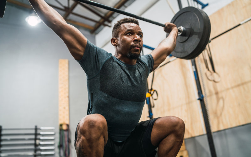 Man in the receiving position of a squat snatch in a CrossFit style gym.