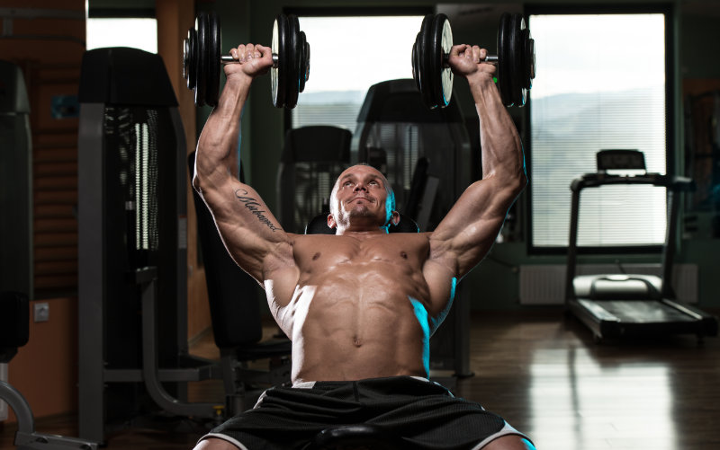 Shirtless man doing incline bench press in a commercial gym. 