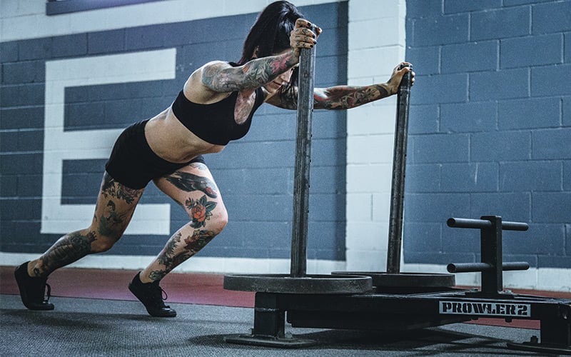 Lean athletic female doing sled pushes in the gym