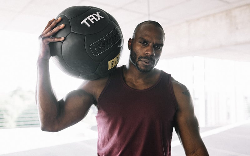Muscular African American man holding a medicine ball on his shoulders