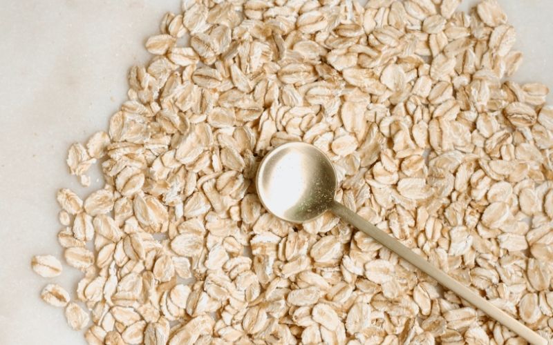 Uncooked oats spread on marble counter with gold spoon on top.