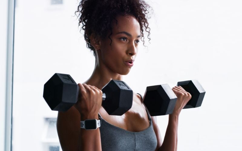 Lean female doing dumbbell bicep curls.