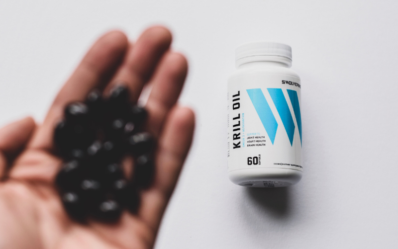 Top-down image of a hand full of black pills in front of a bottle of Swolverine krill oil.