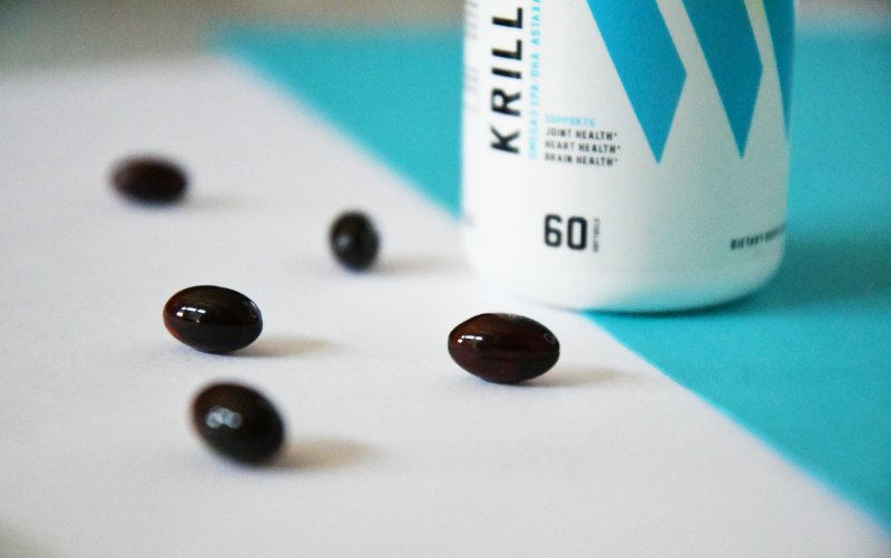 Styled product shot of black capsules in front of a Swolverine Krill Oil bottle. 