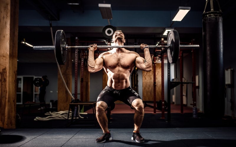Man doing overhead press with barbell in gym setting. 