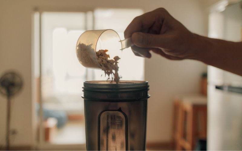 Close up shot of someone pouring protein powder into a shaker bottle in the kitchen.