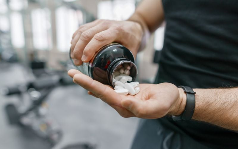 Close up of a fit man holding his supplements in the gym.