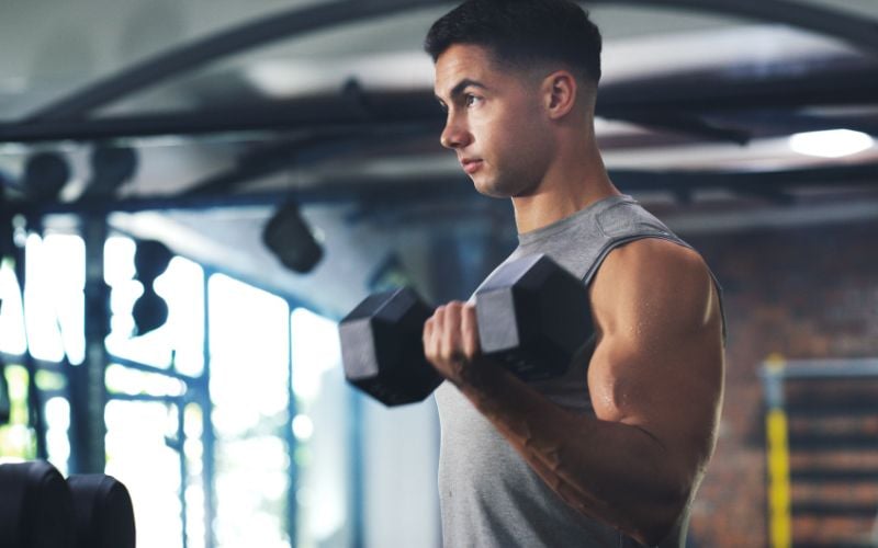 Side profile shot of a muscular man doing dumbbell bicep curls in the gym.