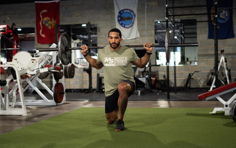 Muscular man doing walking barbell lunges in the gym.