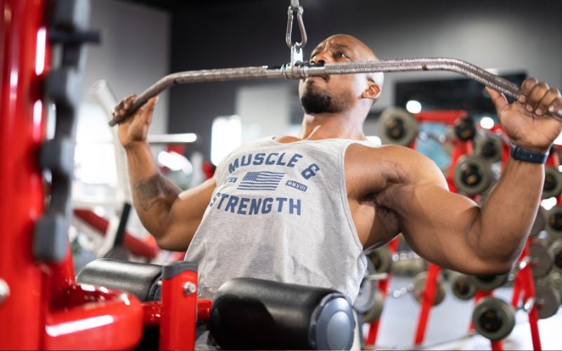 Muscular man wearing a stringer tank doing lat pulldowns in the gym.