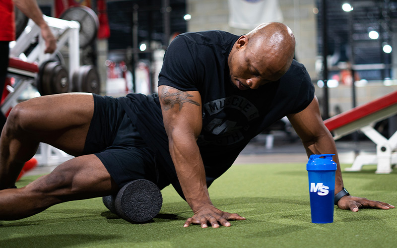 Muscular man wearing a black t-shirt foam rolling in the gym.