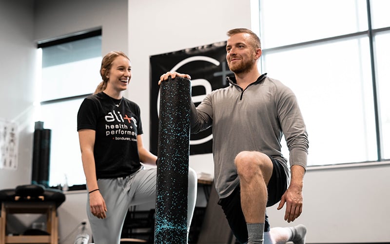 Fit man doing lower body stretches with a coach in the gym.