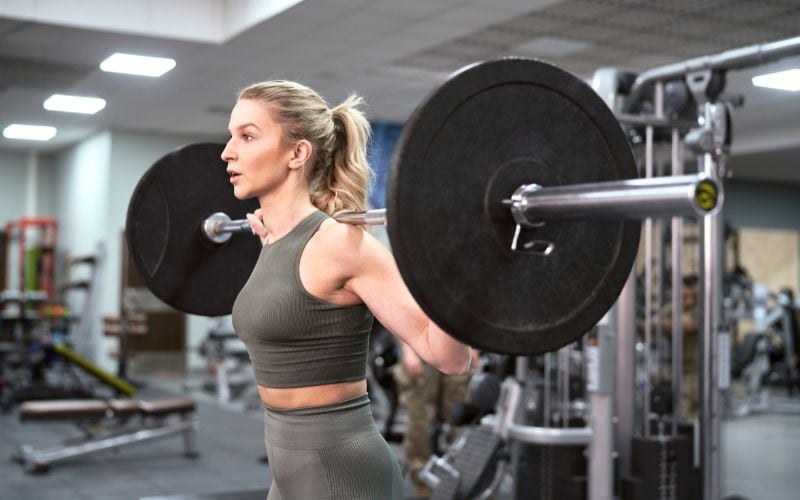 Strong female doing a barbell back squat in the gym.