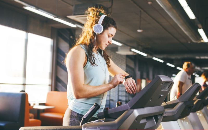 Fit female doing cardio in the gym and wearing a watch to monitor heart rate variability.