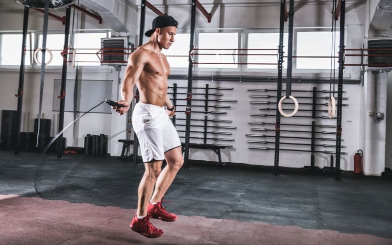 Lean shirtless man doing jump ropes in the gym.