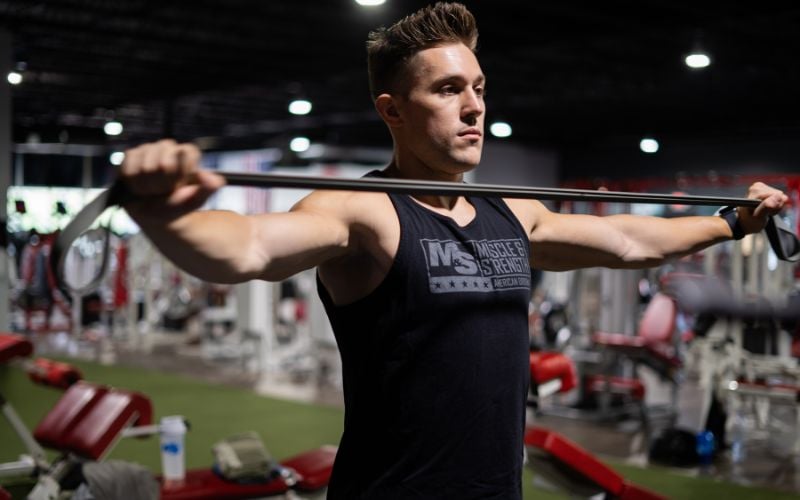 Lean muscular man doing upper body banded stretches in the gym.