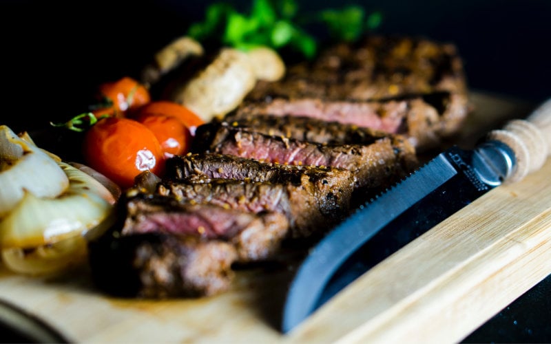 Sliced steak on wood cutting board.