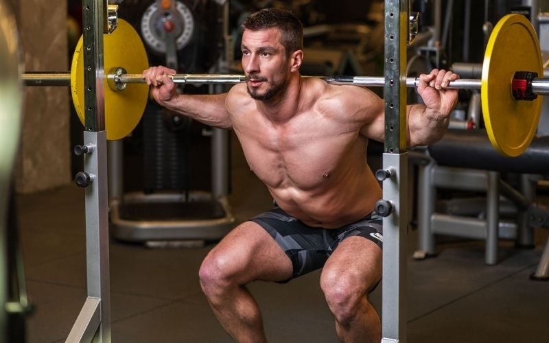 Man doing barbell squat in a gym.