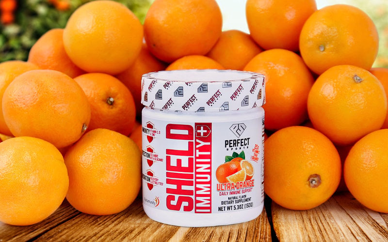 Product shot of Perfect Sports SHIELD Immunity in front of stack of oranges on wooden table.