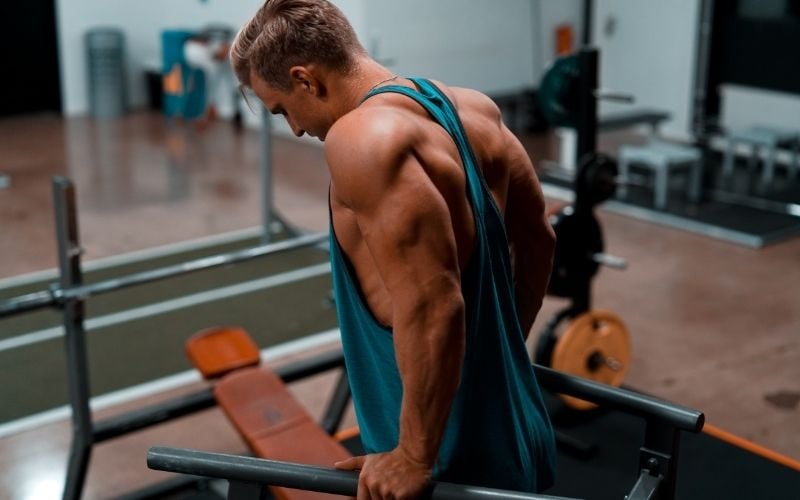 Muscular man in blue tank top doing tricep dips.