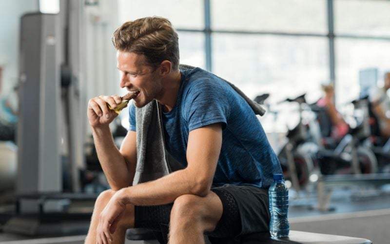 Fit man eating a protein bar in the gym.