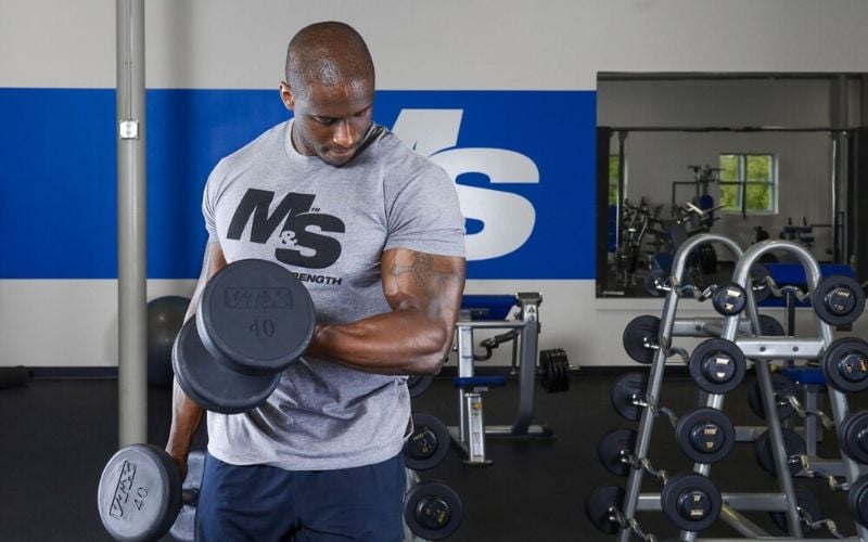 Muscle & Strength Athlete Doing Bicep Curls in Gym