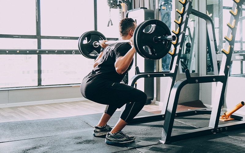 Rear view shot of a man doing barbell squats in the gym