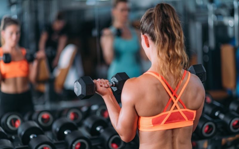 Rear shot of a female doing dumbbell bicep curls in the gym.