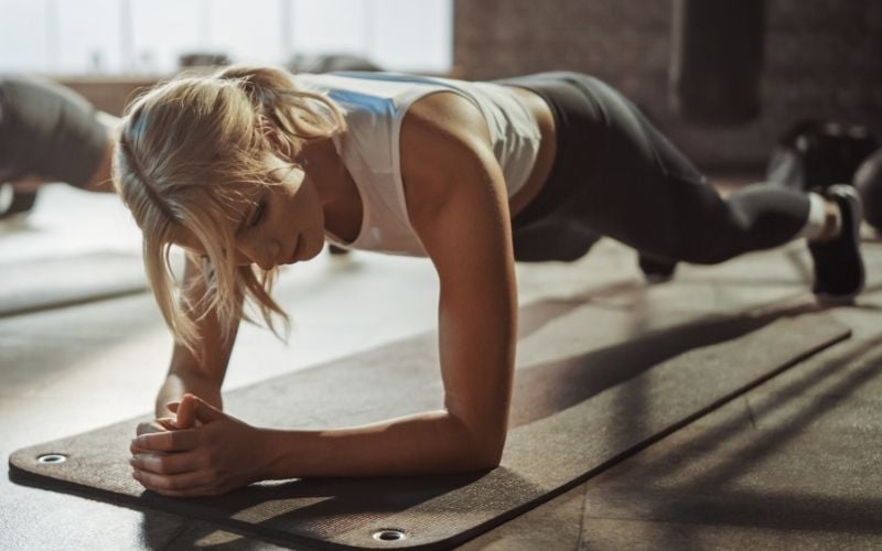 Blonde woman doing forearm plank on yoga mat. 