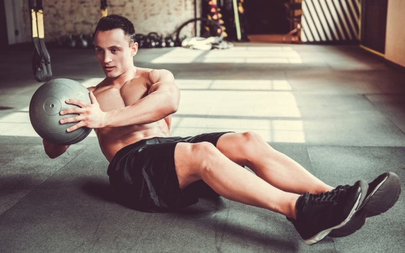 Man doing russian twist with medicine ball.