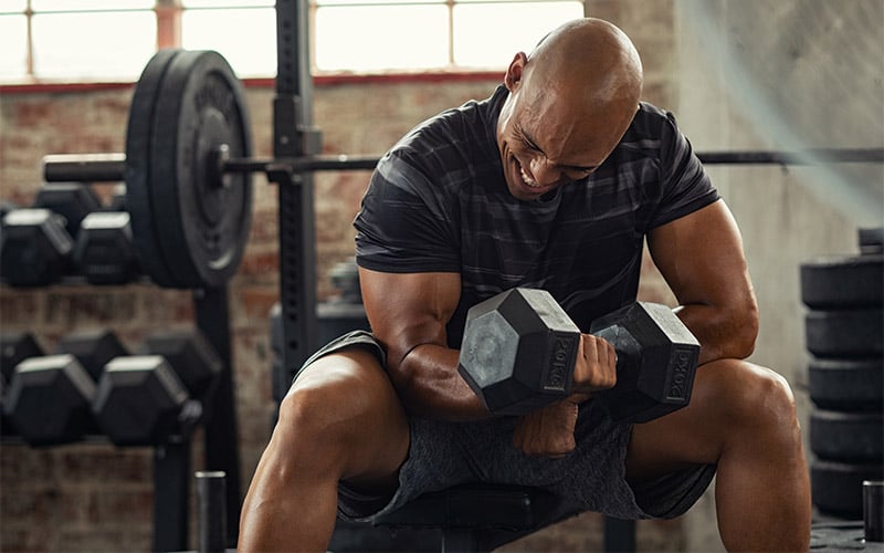 Strong man in black striped shirt performing dumbbell concentration curl