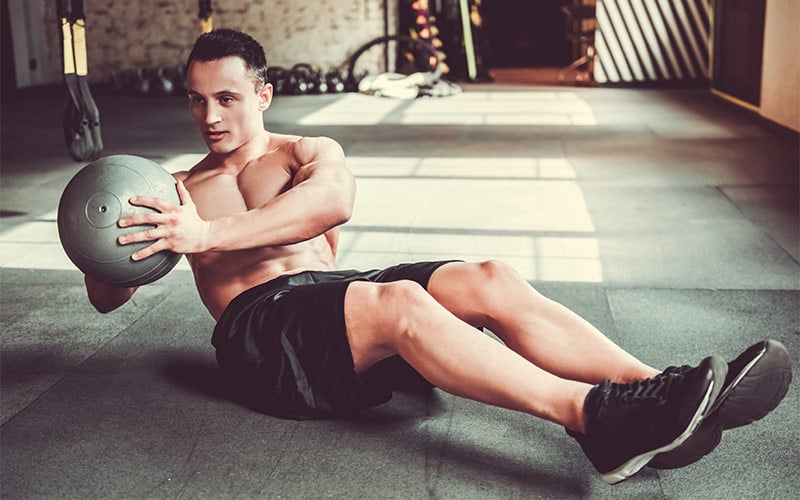 Muscular man performing medicine ball russian/mason twists