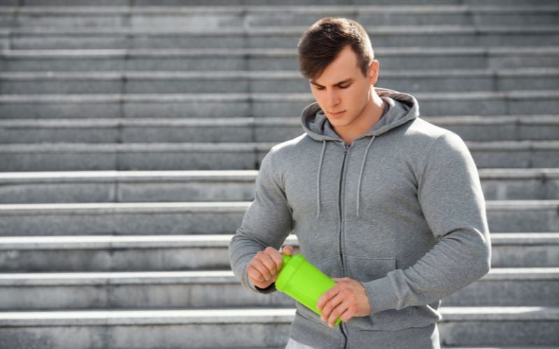 Muscular man holding a protein shaker bottle outside.