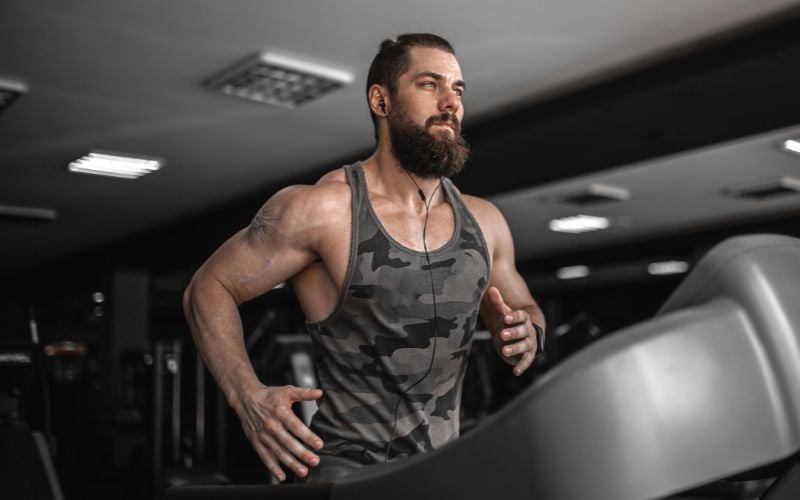 Muscular man wearing a black tank top listening to music while running on the treadmill