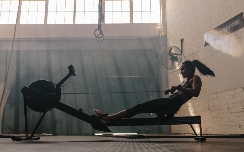 Side profile shot of a fit brunette female rowing in the gym