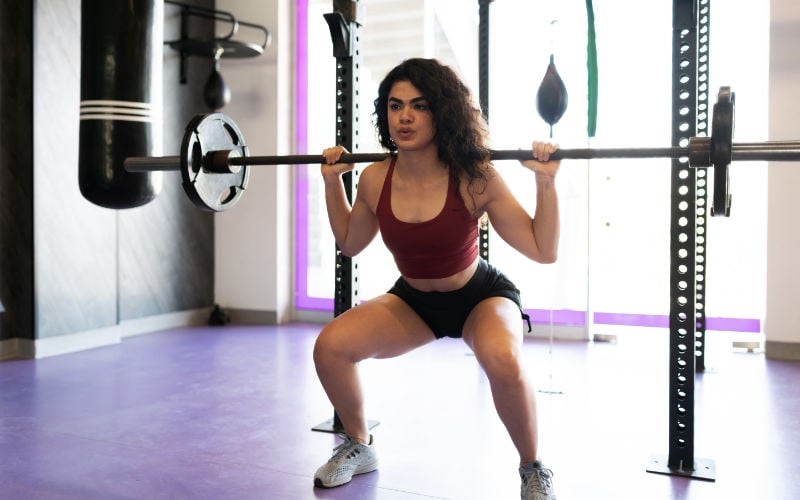 Woman doing barbell back squats in gym.