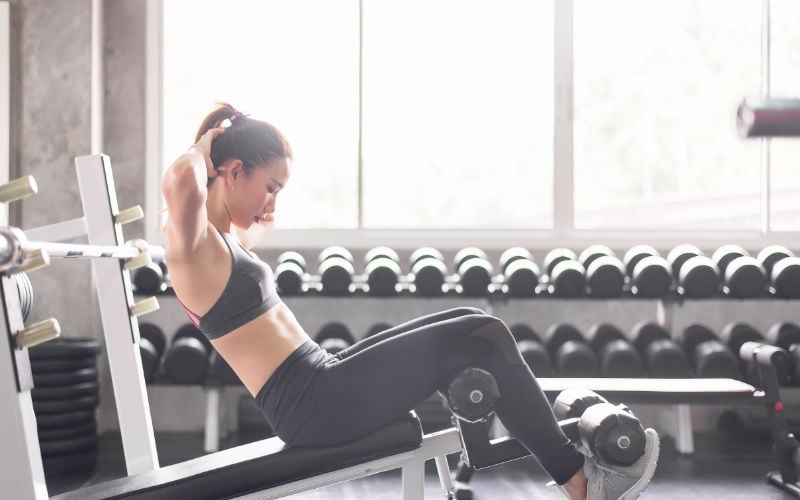 Woman doing decline sit ups in gym. 