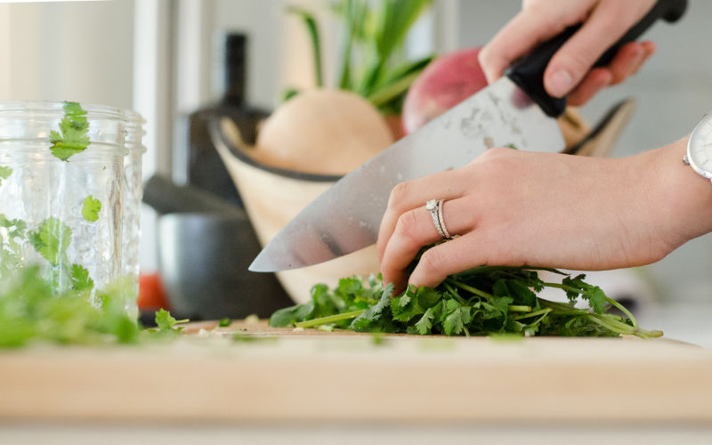 Close up of woman's hands as she chops cilantro on a wooden cutting board.
